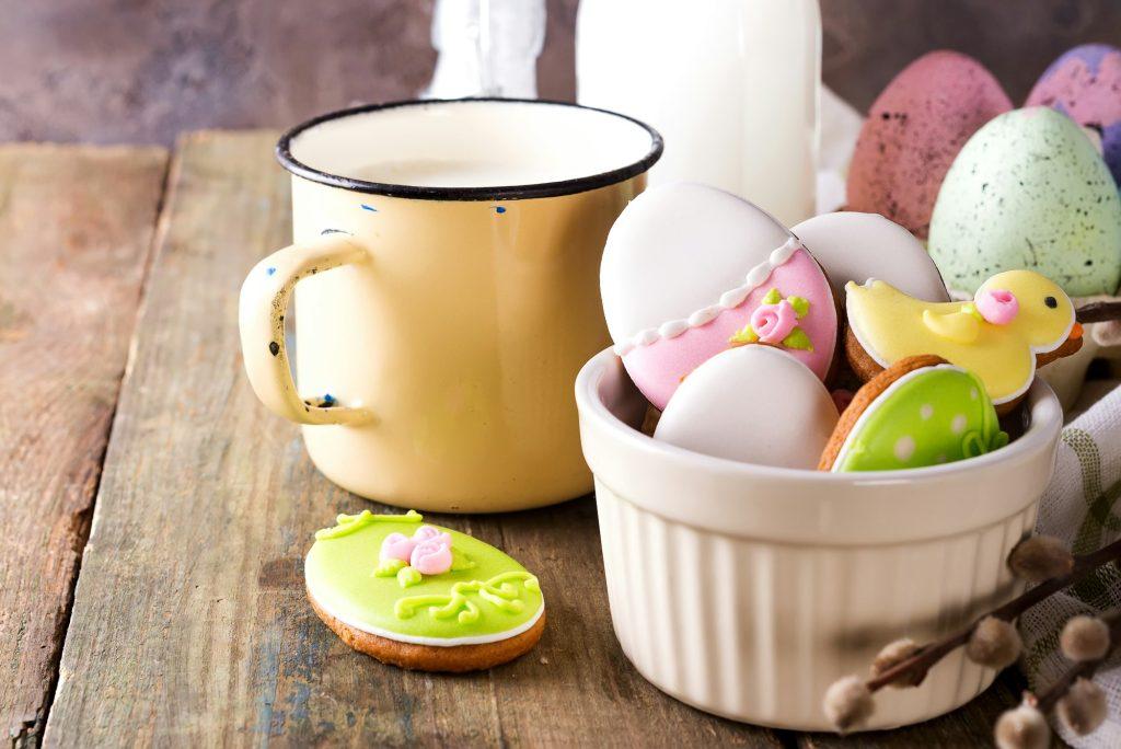 Eggs shaped Easter cookies, hand-made with cup of milk. Decorated with fondant icing on old wooden